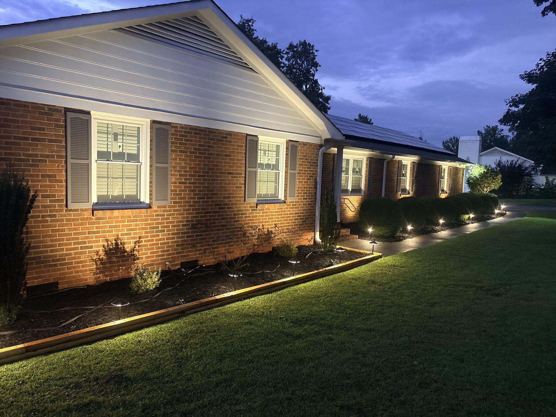 LED path lighting along a walkway and brick foundation beds at dusk — landscape lighting installation Greenville SC by Iron Lungs