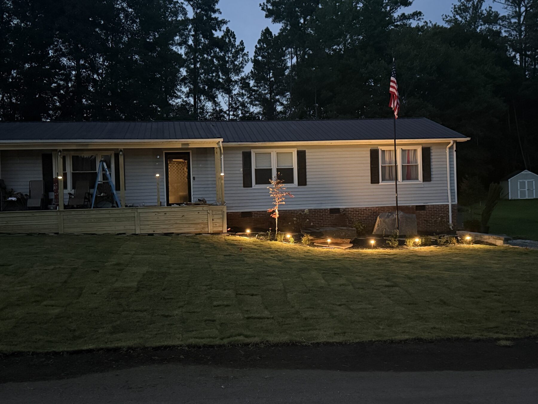 Freshly installed sod on a front lawn at dusk with the seams still visible, plus a new stone-bordered planting bed and landscape lighting — Iron Lungs Grading sod installation, Greenville SC